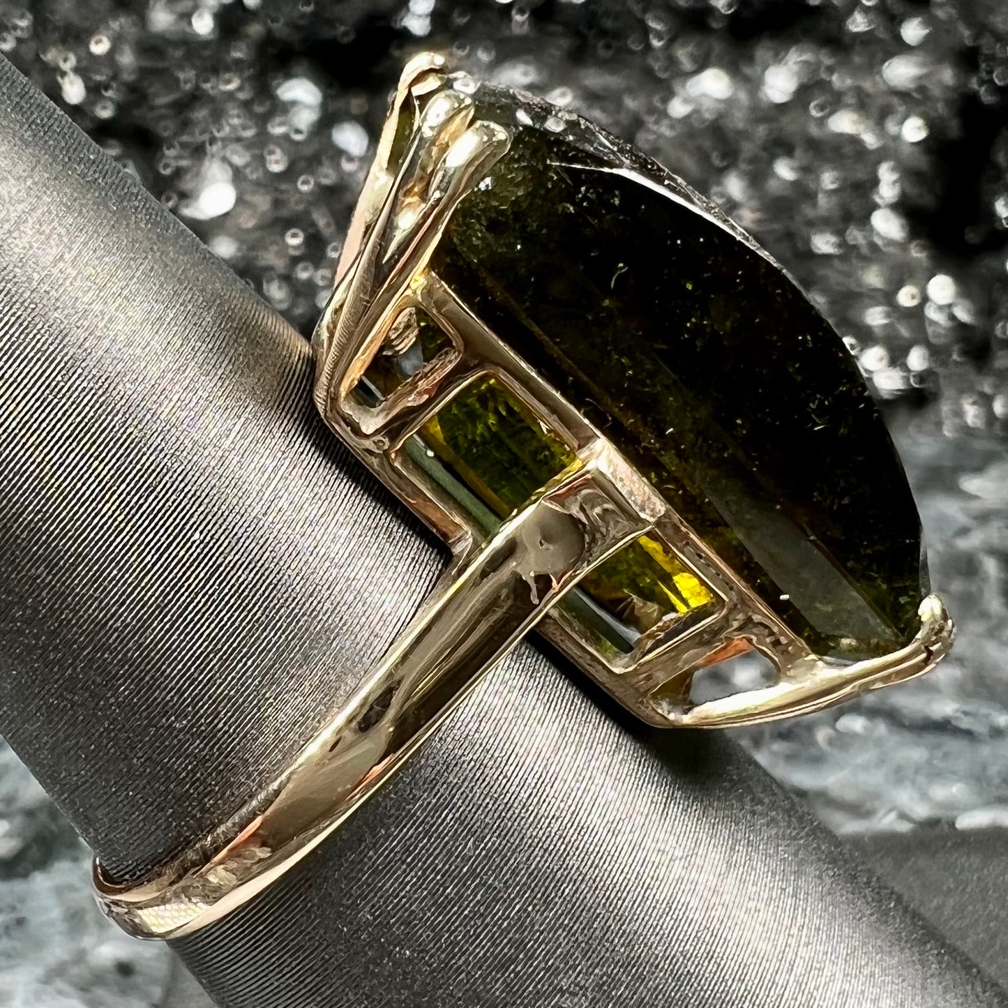 A faceted step-cut dark green tourmaline basket set solitaire ring cast in yellow gold.