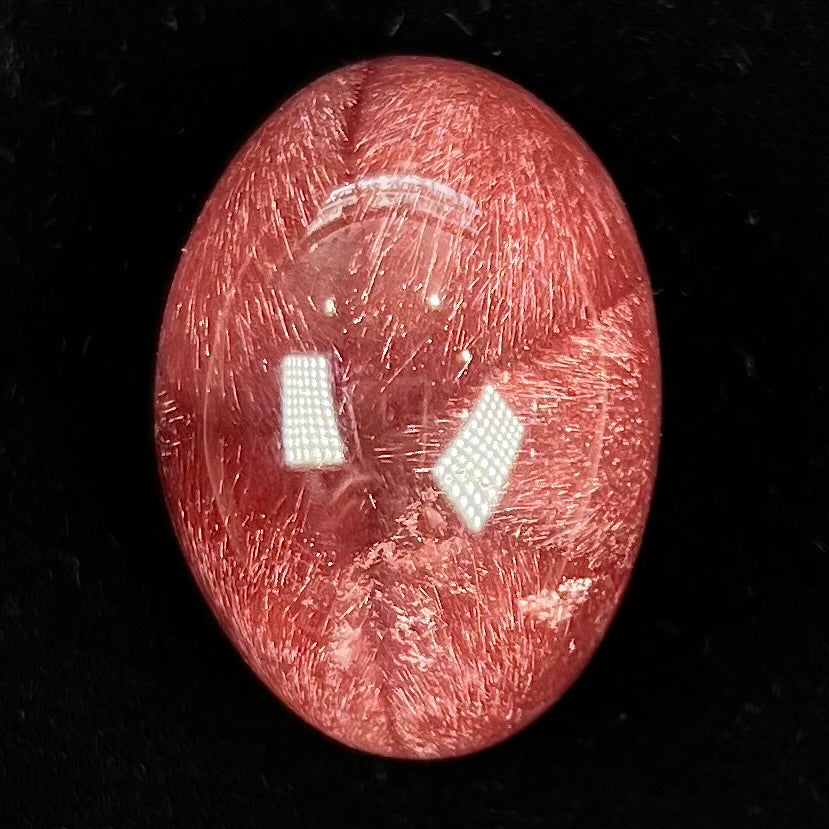 A large, oval cabochon cut strawberry quartz.  The stone has a trapiche star-like pattern.