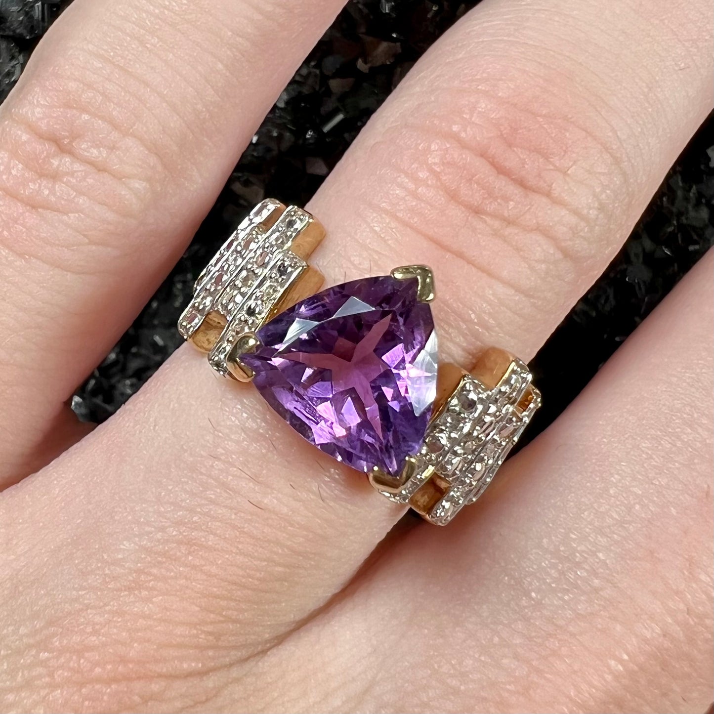 A yellow gold ring set with a trillion cut amethyst and round diamond accent stones.