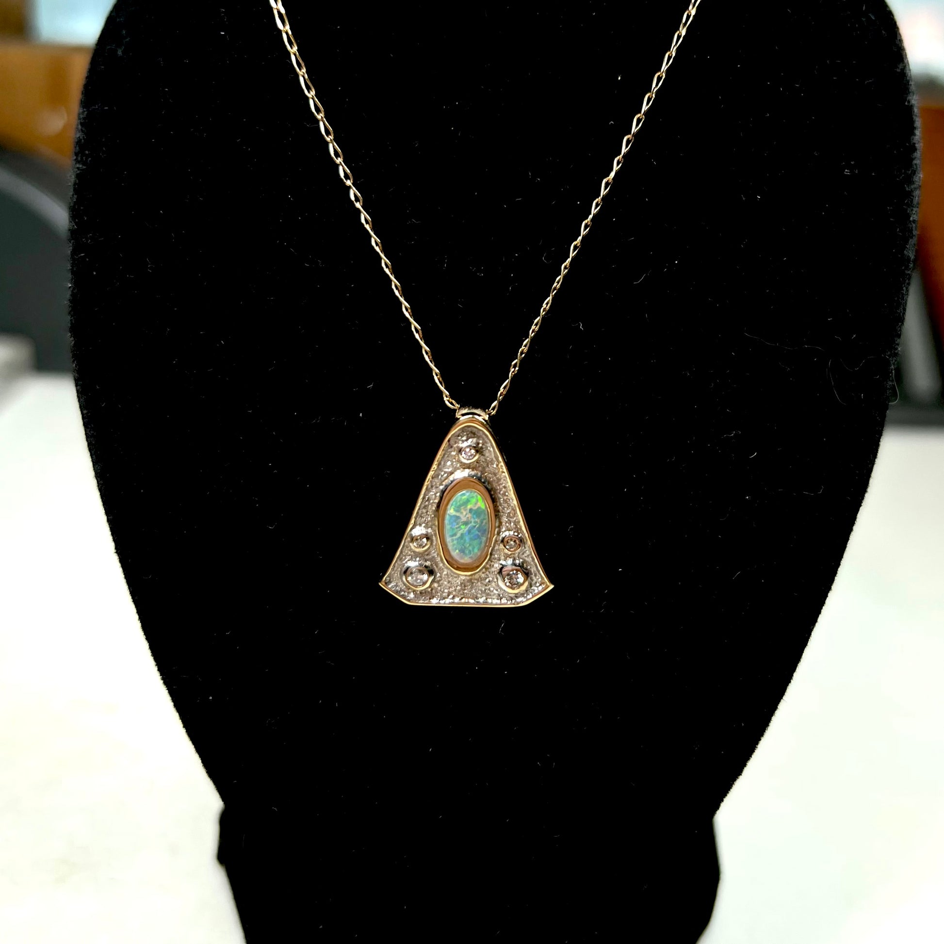 A triangular gold pendant set with five round diamonds and a white crystal opal with green fire.