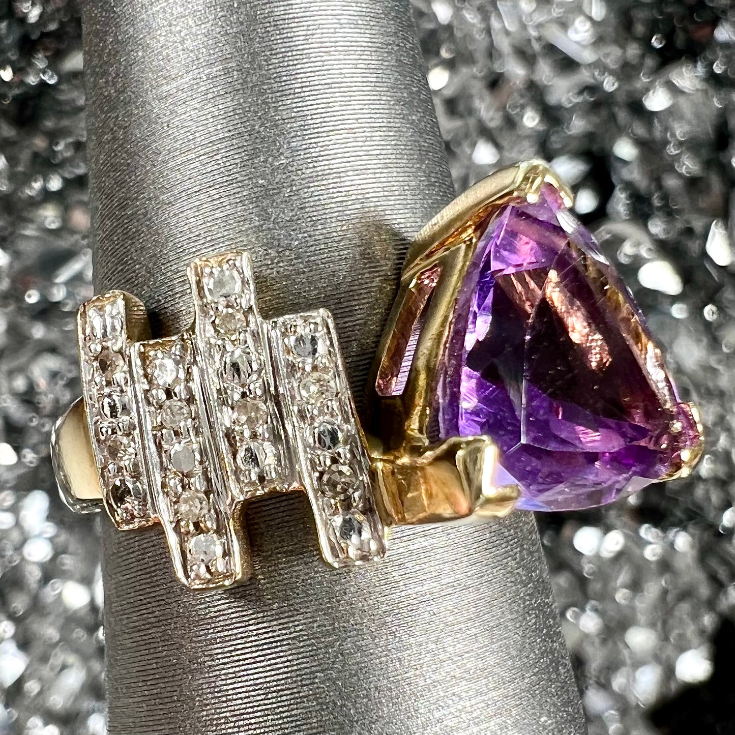 A yellow gold ring set with a trillion cut amethyst and round diamond accent stones.