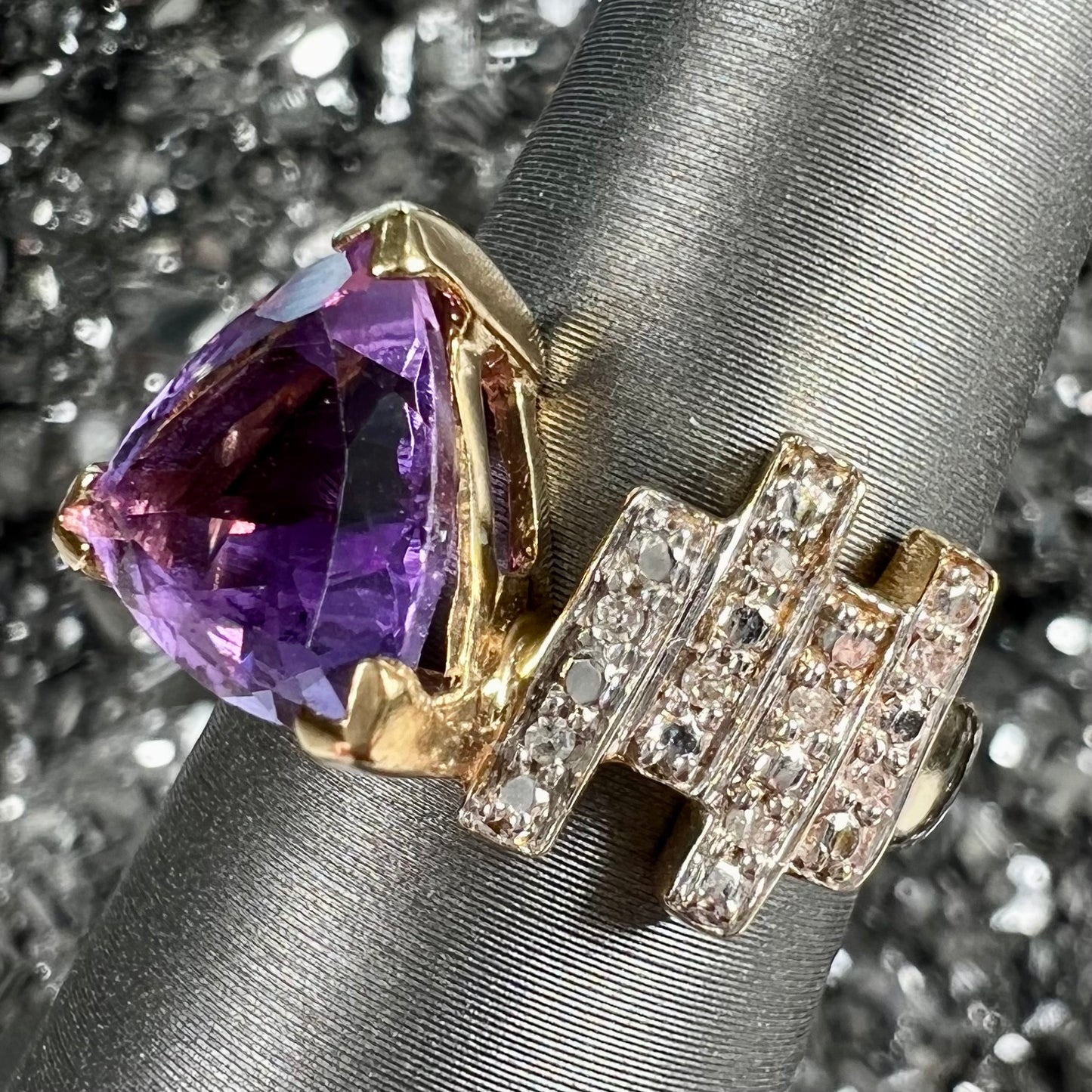 A yellow gold ring set with a trillion cut amethyst and round diamond accent stones.