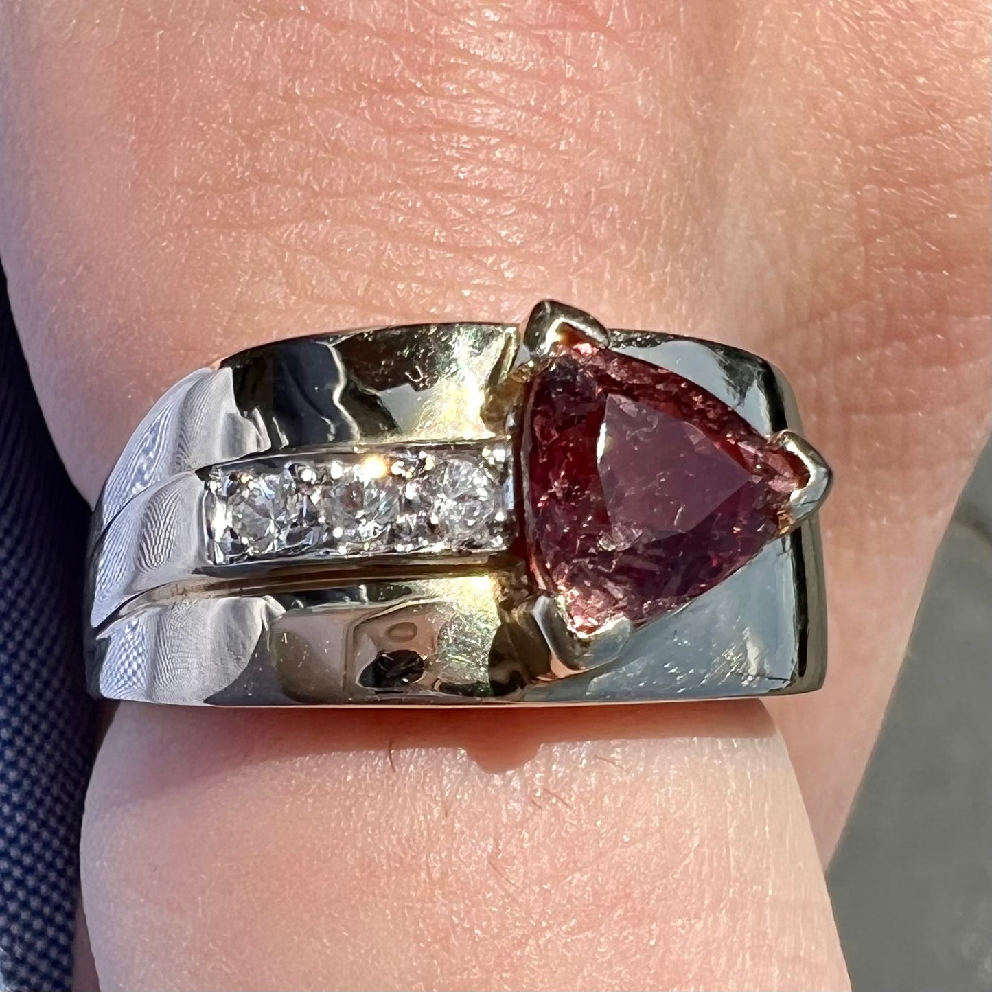 A men's gold pink tourmaline ring.  Set next to the trillion cut tourmaline is a row of three round white sapphires.