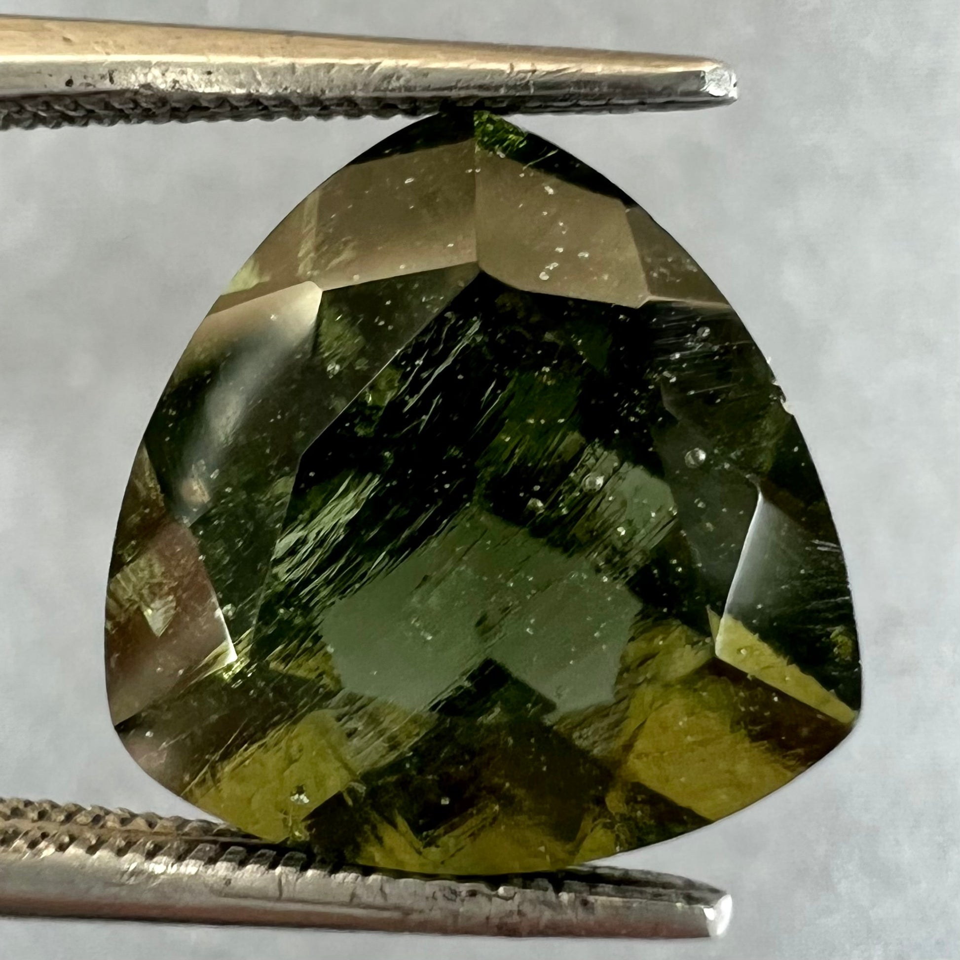 A loose, faceted trillion cut moldavite stone that weighs 2.73 carats.