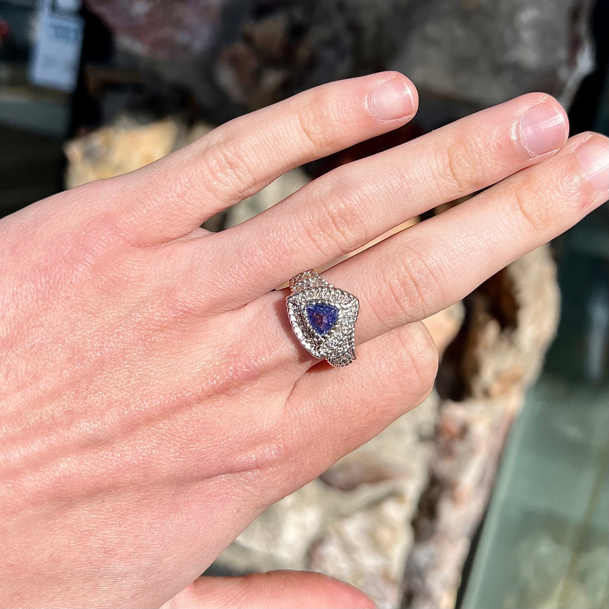 A white gold trillion cut tanzanite ring set with a diamond halo and diamond accents.