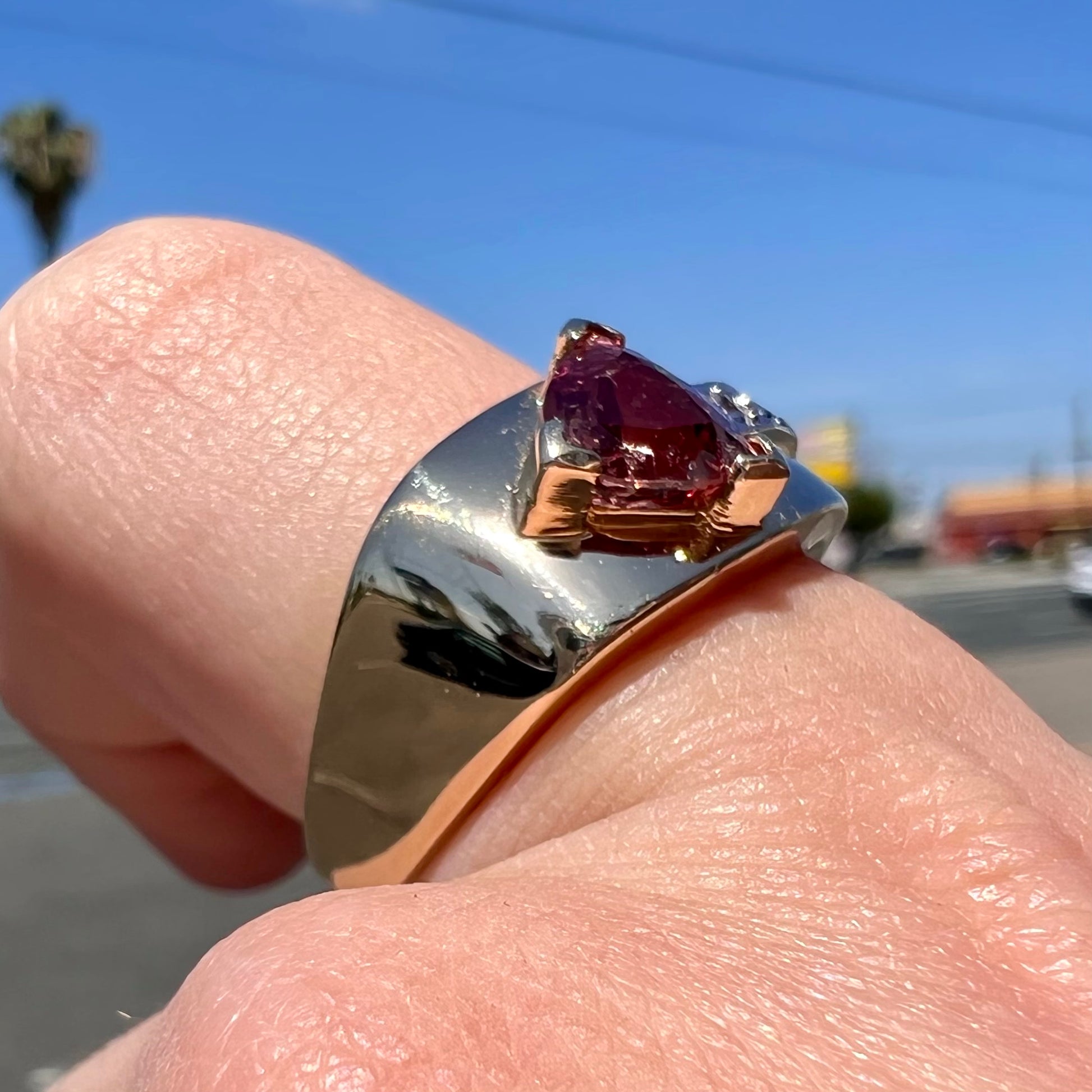 A men's gold pink tourmaline ring.  Set next to the trillion cut tourmaline is a row of three round white sapphires.