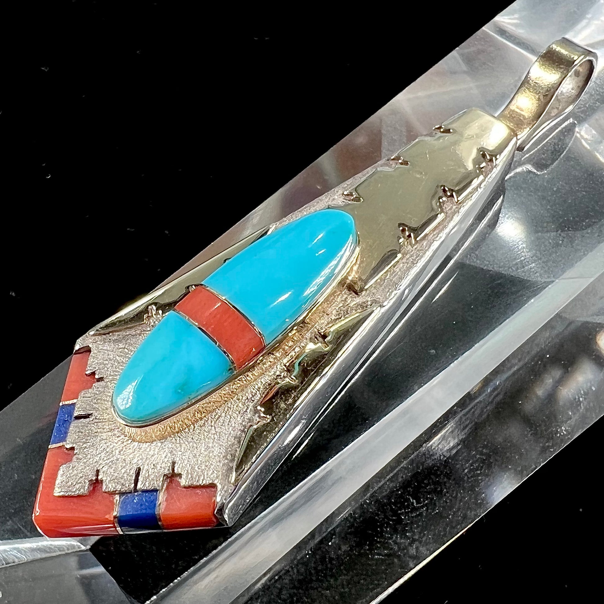 A yellow gold and sterling silver pendant inlaid with turquoise, coral, and lapis lazuli stones.  The piece is made by an unknown Native American artist and signed with the initials "LY".
