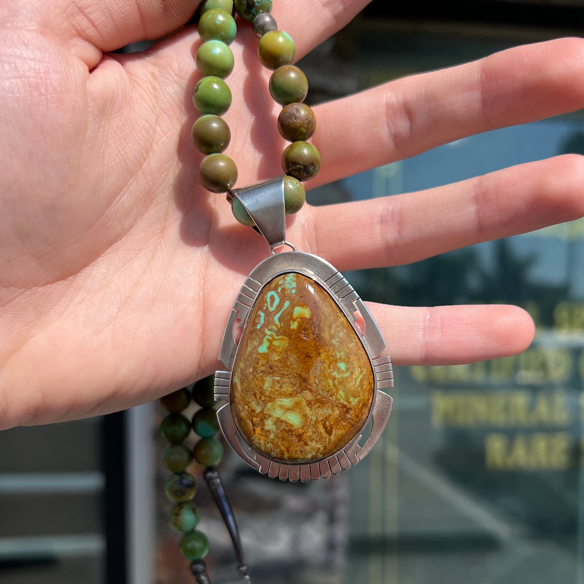 A handmade, likely Navajo silver pendant set with Kingman turquoise on a green Kingman turquoise beaded necklace.