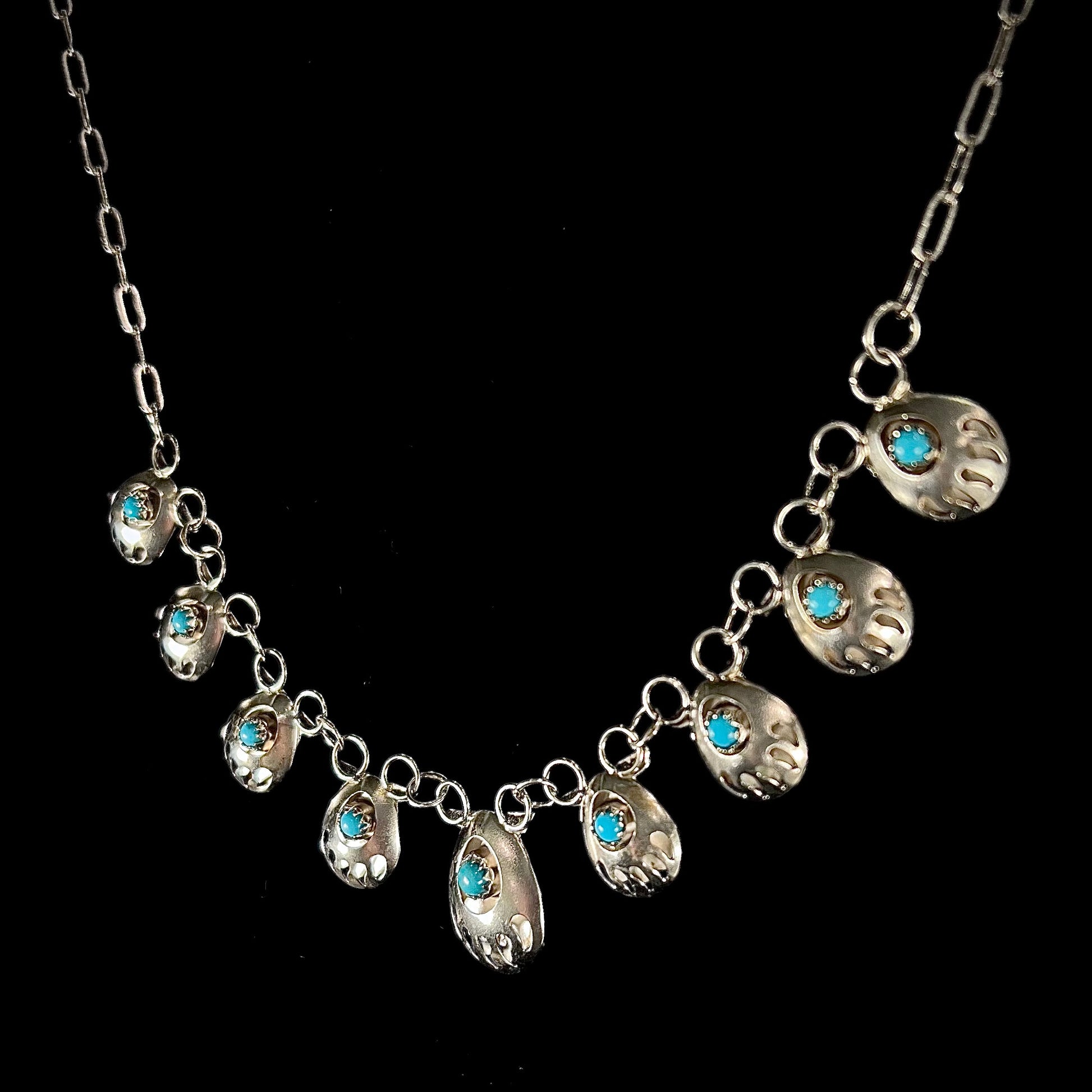 A silver turquoise necklace handmade with nine silver bear paws set with round turquoise stones.
