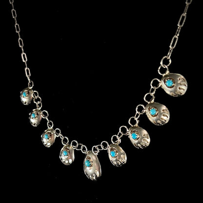 A silver turquoise necklace handmade with nine silver bear paws set with round turquoise stones.