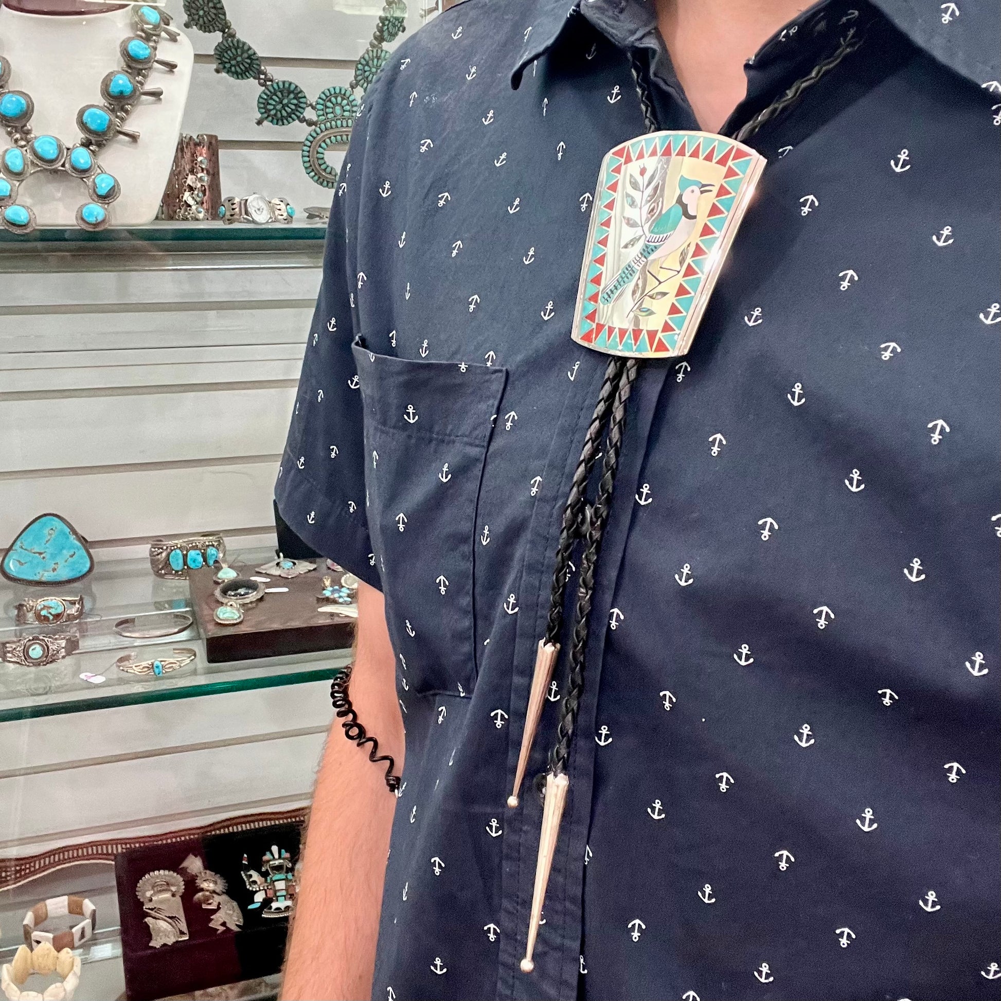 A turquoise and coral inlay bolo tie featuring the motif of a blue jay bird, handmade by Zuni artists Dennis and Nancy Edaakie.