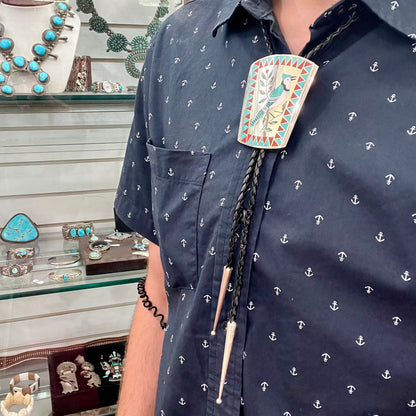 A turquoise and coral inlay bolo tie featuring the motif of a blue jay bird, handmade by Zuni artists Dennis and Nancy Edaakie.