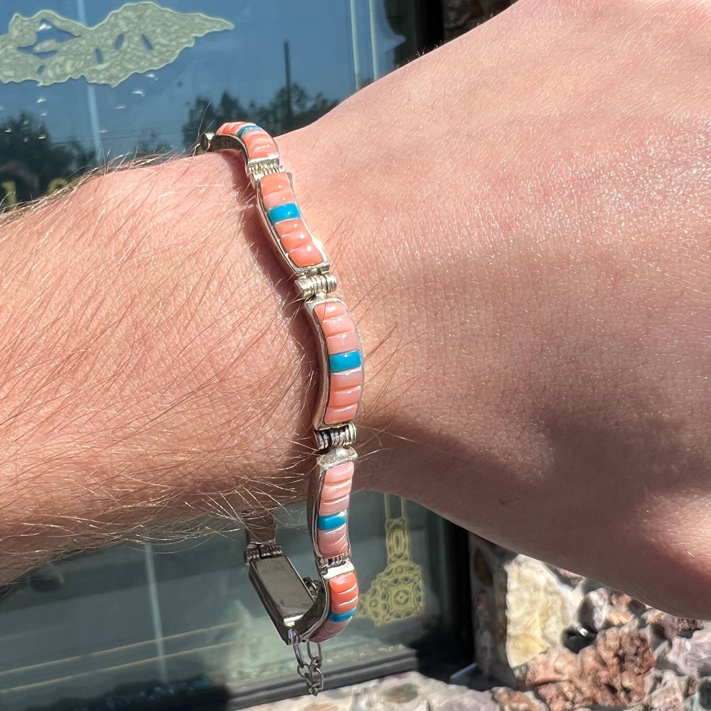 A ladies' sterling silver tennis style bracelet set with polished pink coral and turquoise inlay.