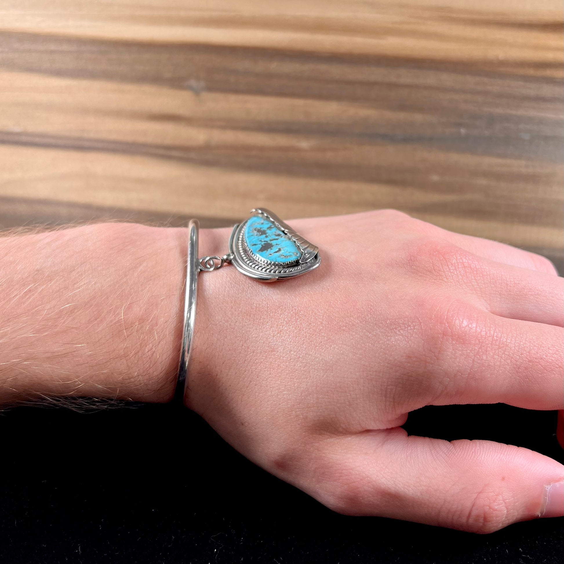 A sterling silver cuff bracelet with an attached dangle segment set with a turquoise stone from Pinto Valley.