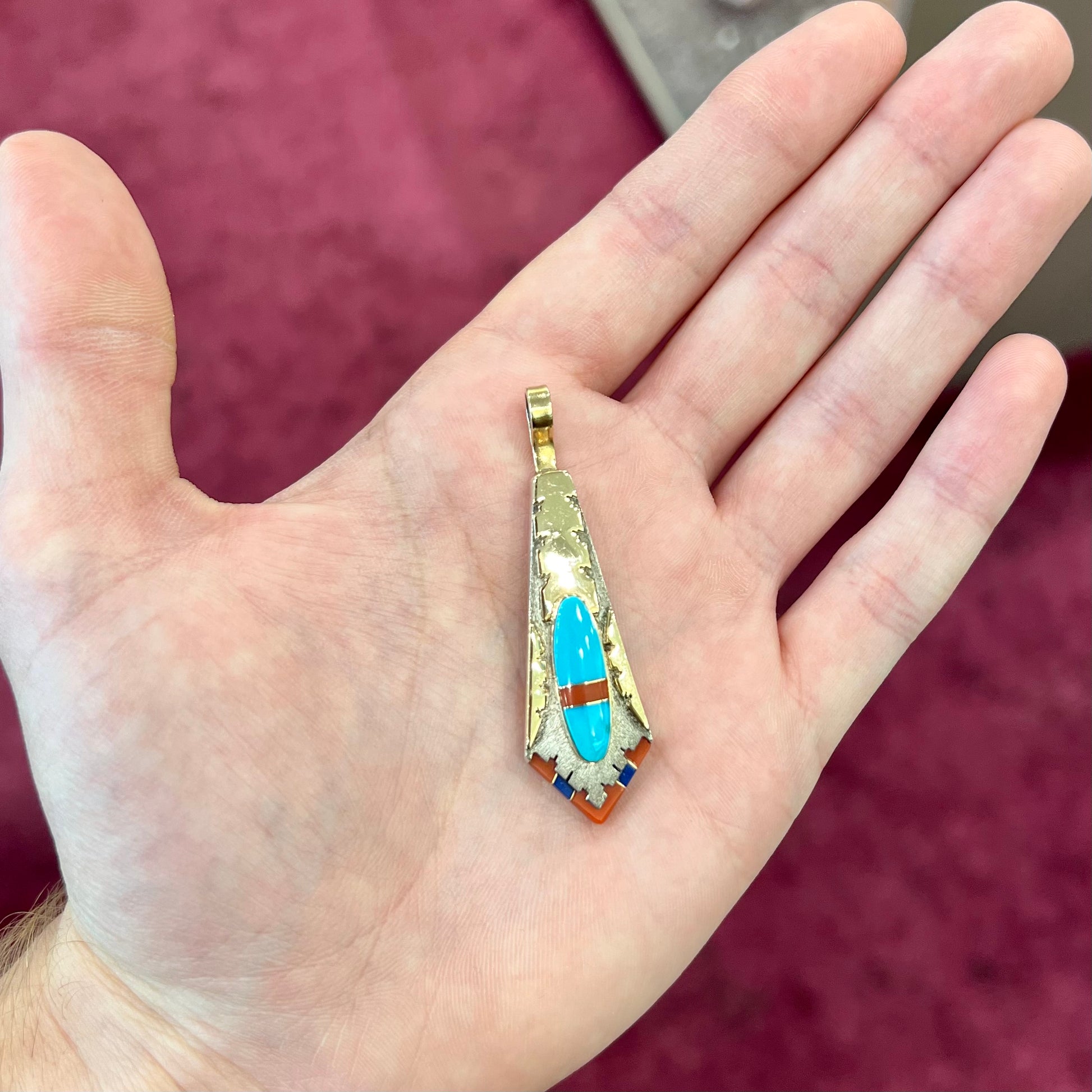 A yellow gold and sterling silver pendant inlaid with turquoise, coral, and lapis lazuli stones.  The piece is made by an unknown Native American artist and signed with the initials "LY".