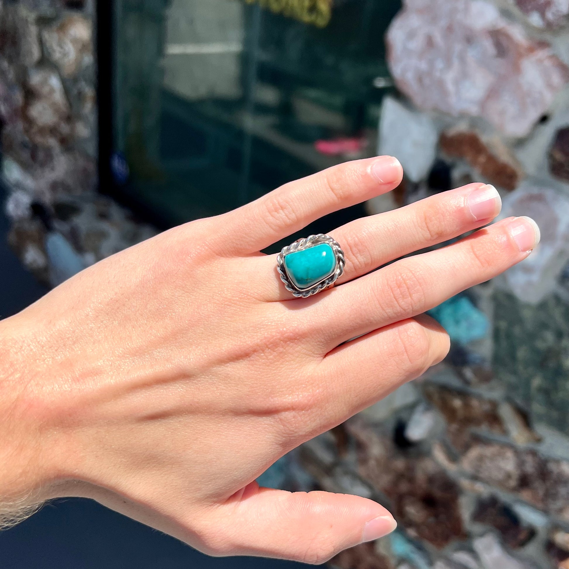A sterling silver turquoise split shank ring.  There is a handmade silver rope around the turquoise.