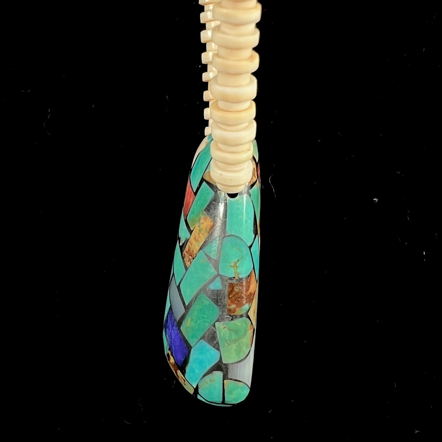A three dimensional mosaic stone inlay pendant set with turquoise, lapis lazuli, coral, and mother of pearl on a puka shell necklace.