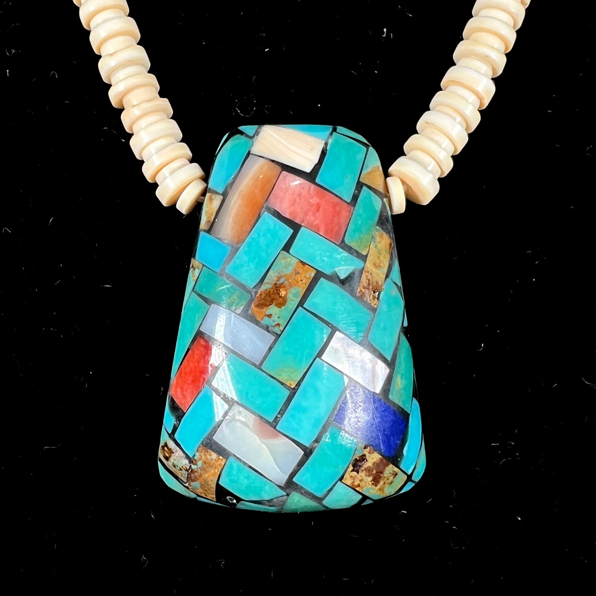 A three dimensional mosaic stone inlay pendant set with turquoise, lapis lazuli, coral, and mother of pearl on a puka shell necklace.