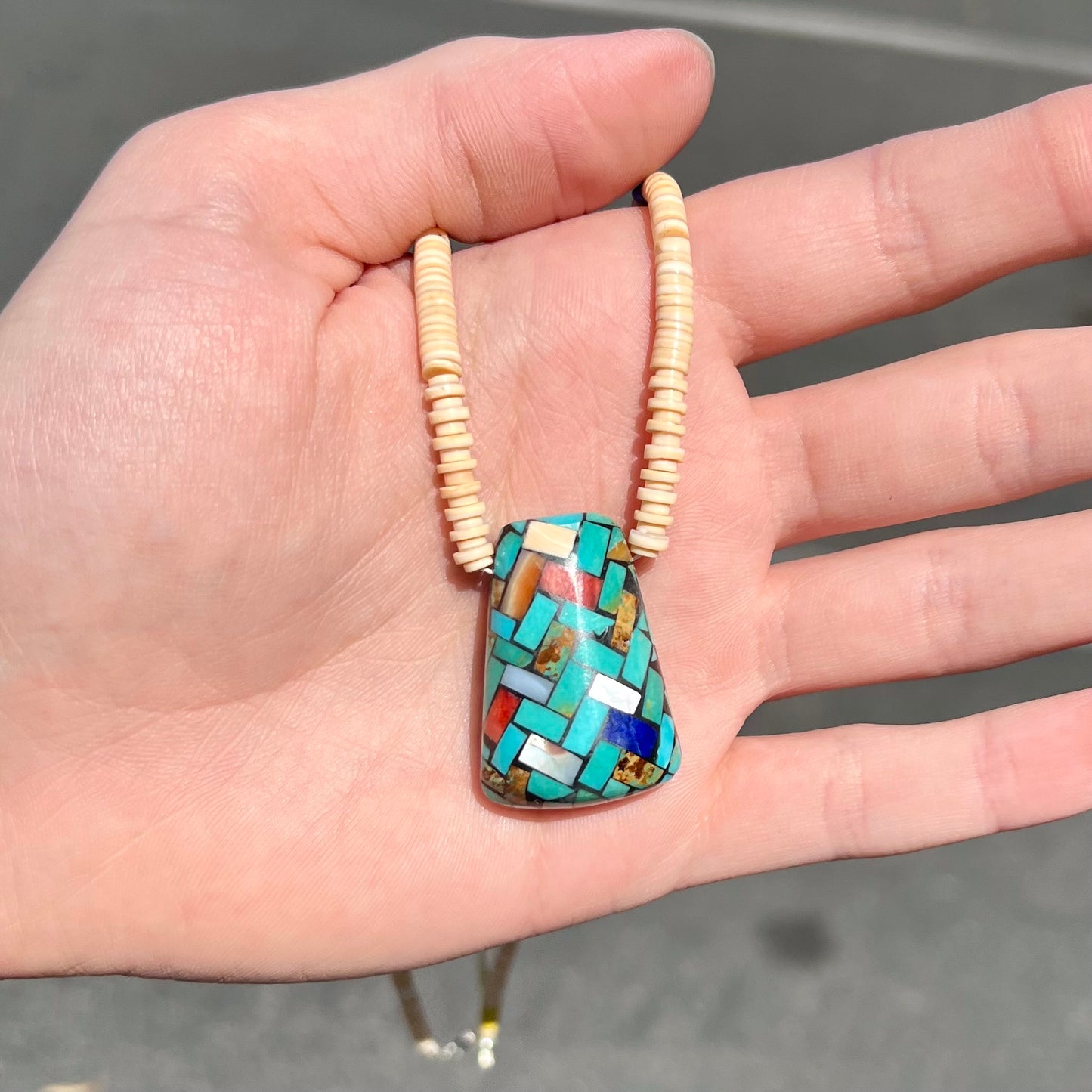 A three dimensional mosaic stone inlay pendant set with turquoise, lapis lazuli, coral, and mother of pearl on a puka shell necklace.