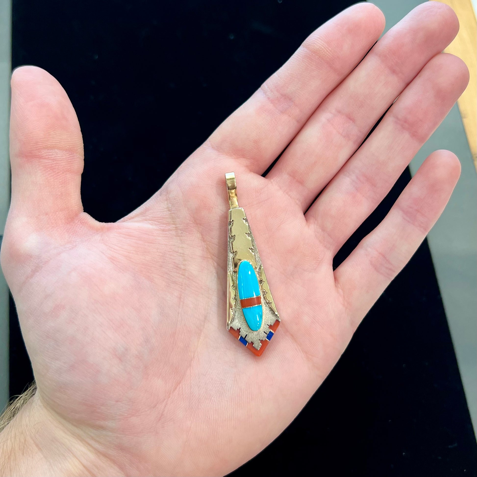 A yellow gold and sterling silver pendant inlaid with turquoise, coral, and lapis lazuli stones.  The piece is made by an unknown Native American artist and signed with the initials "LY".