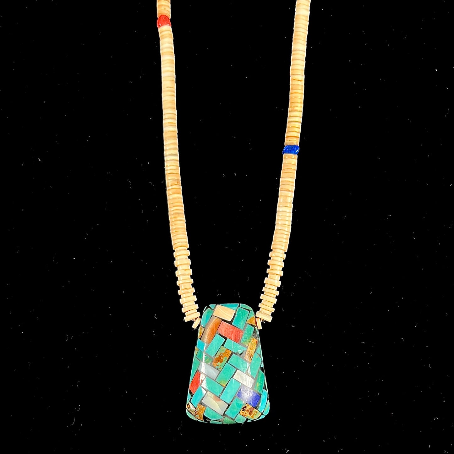 A three dimensional mosaic stone inlay pendant set with turquoise, lapis lazuli, coral, and mother of pearl on a puka shell necklace.