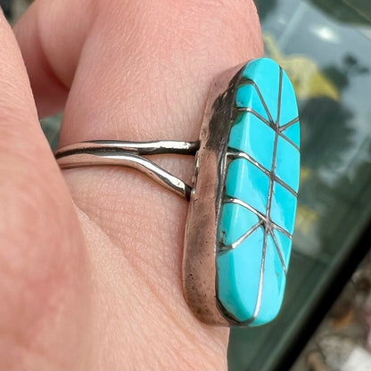 A handmade silver turquoise ring inlaid with six pieces of Sleeping Beauty turquoise.  The back of the ring is signed "FT".