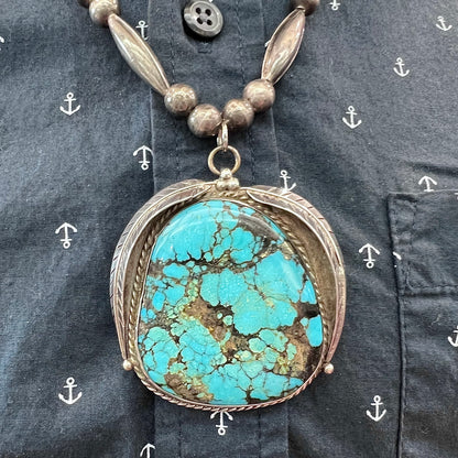 A Navajo style silver beaded necklace set with a Kingman spiderweb turquoise stone.