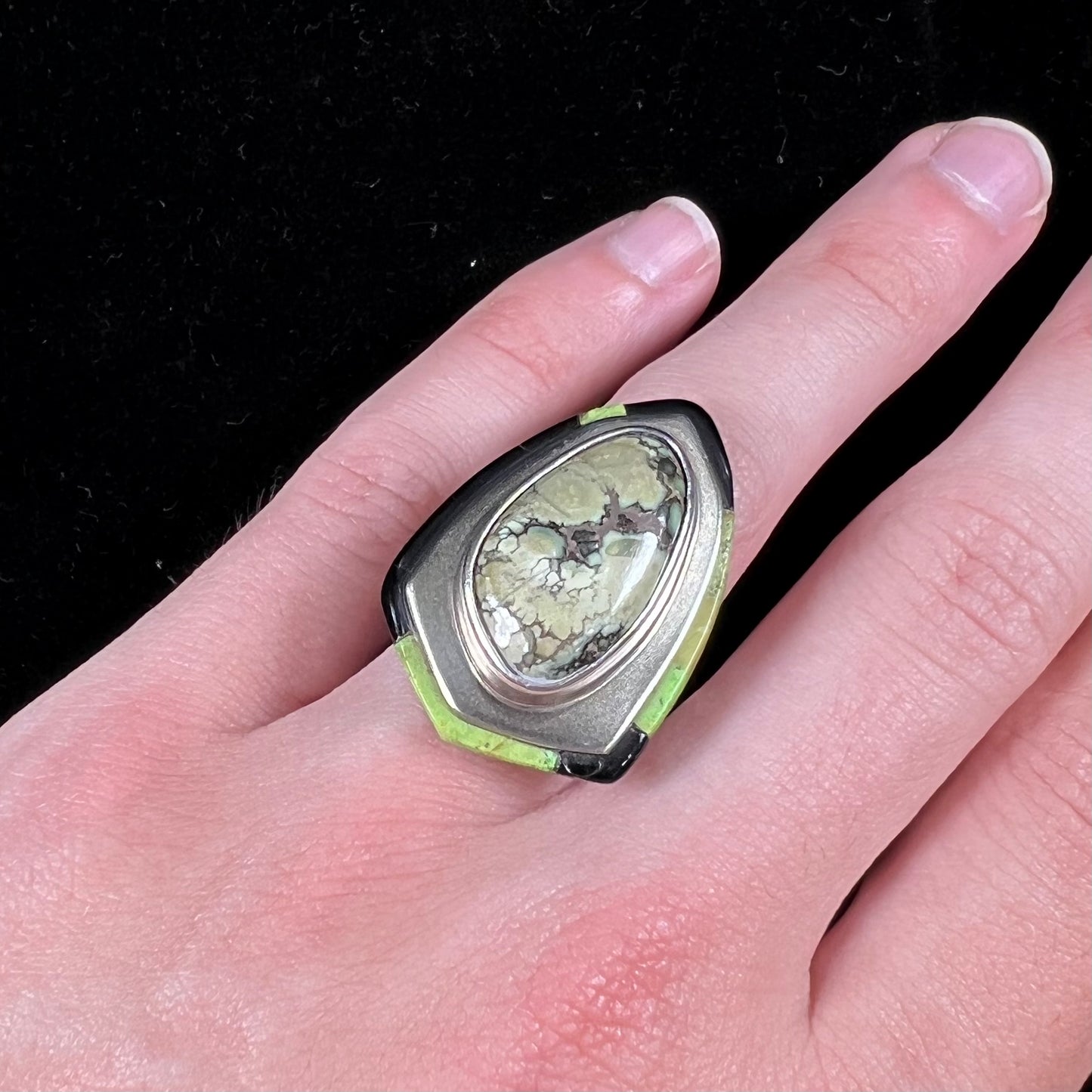 A shield shaped silver ring bezel set with a green gaspeite stone with stone inlaid edges, handmade by artist Benny Armijo.