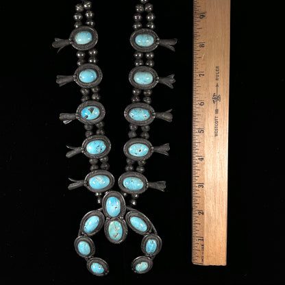 A silver Navajo style unisex squash blossom necklace set with oval cut Sleeping Beauty turquoise stones.