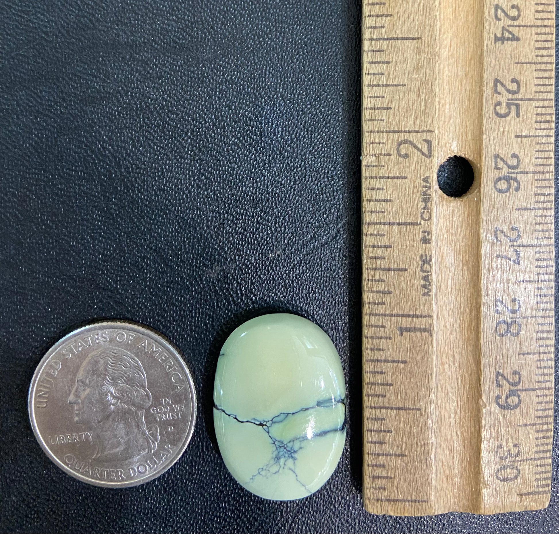 A loose, oval cabochon cut variscite stone from Utah, USA.  The stone is yellow-green with a black matrix.