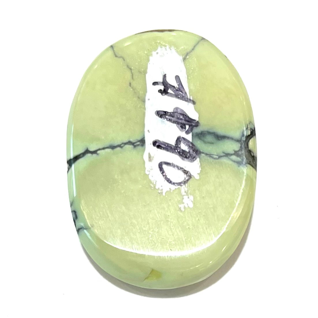A loose, oval cabochon cut variscite stone from Utah, USA.  The stone is yellow-green with a black matrix.