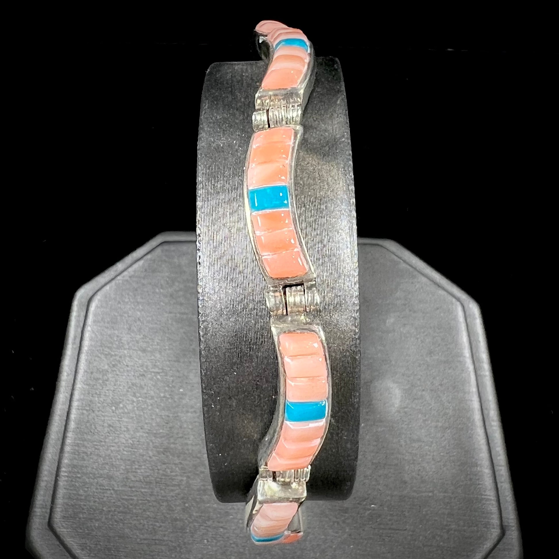 A ladies' sterling silver tennis style bracelet set with polished pink coral and turquoise inlay.