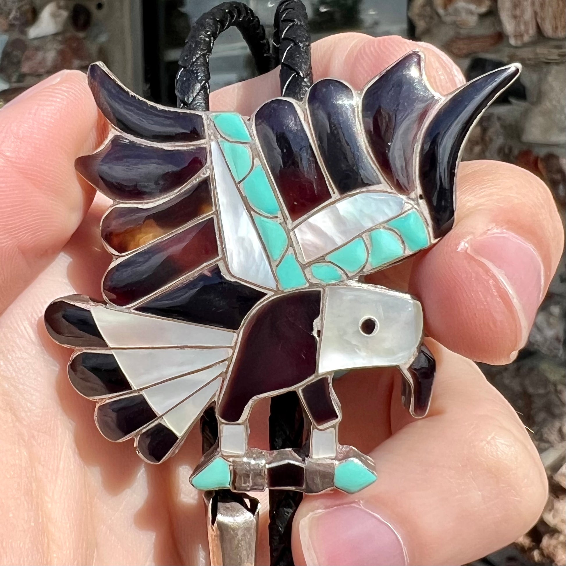 A sterling silver Zuni Indian-made bolo tie featuring the motif of three flying eagles inlaid with natural stones.