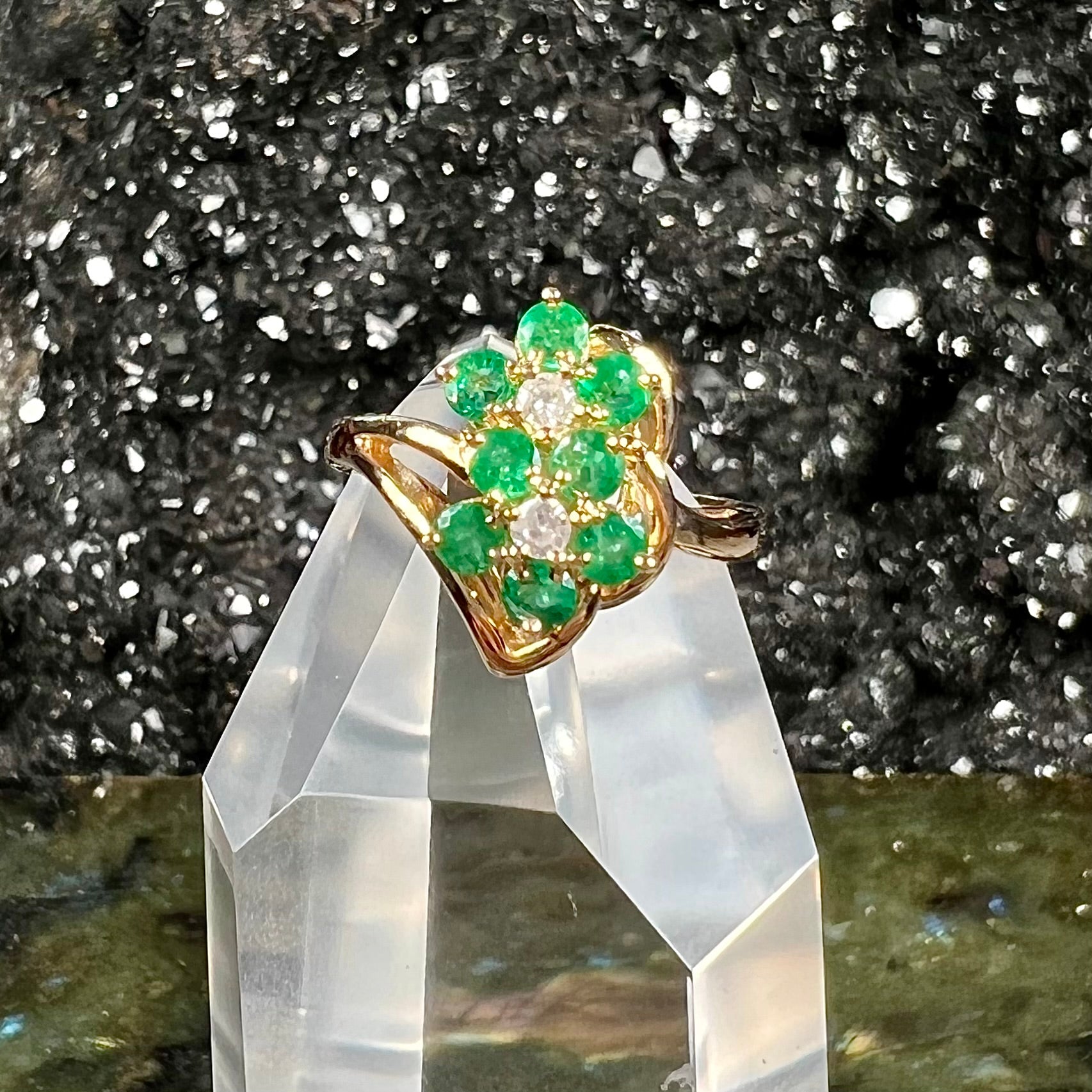 A yellow gold ring set with round cut emerald and diamonds that form the shape of two flowers.