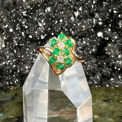 A yellow gold ring set with round cut emerald and diamonds that form the shape of two flowers.
