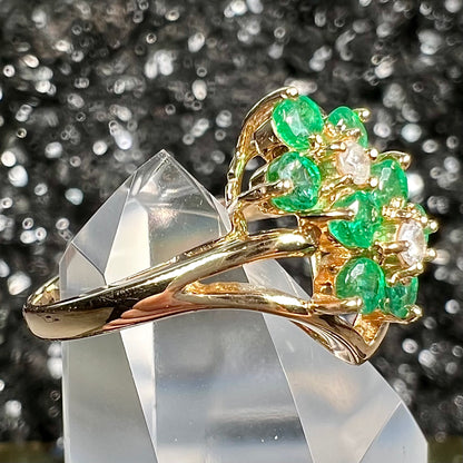 A yellow gold ring set with round cut emerald and diamonds that form the shape of two flowers.