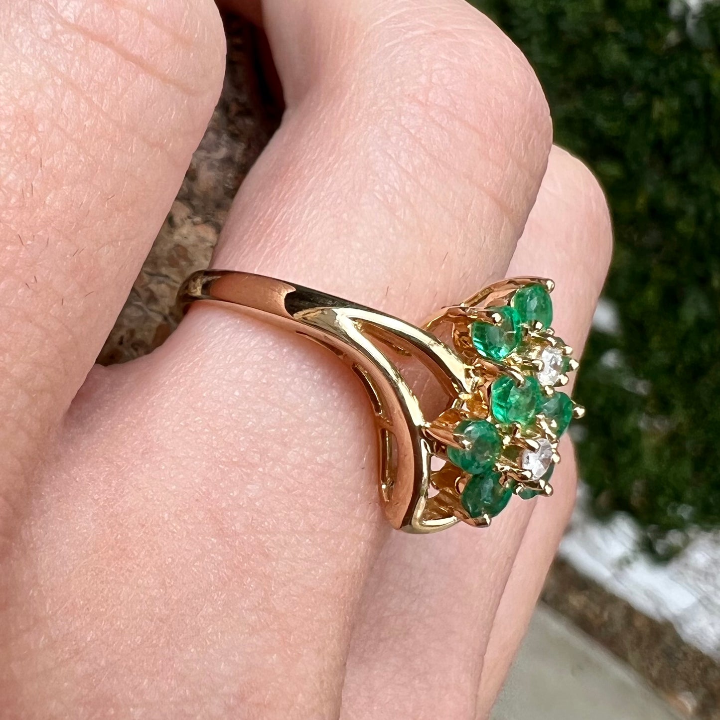 A yellow gold ring set with round cut emerald and diamonds that form the shape of two flowers.