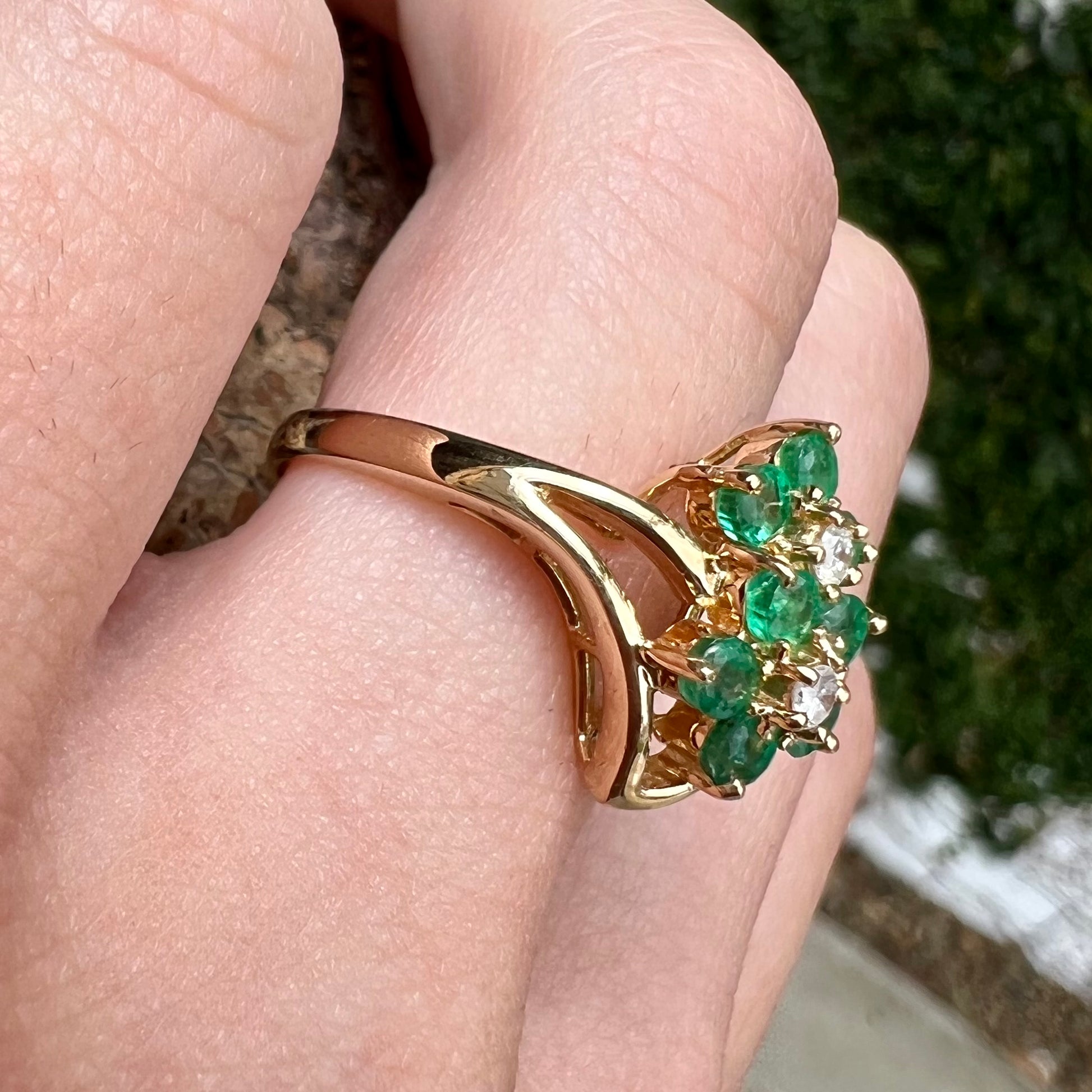 A yellow gold ring set with round cut emerald and diamonds that form the shape of two flowers.
