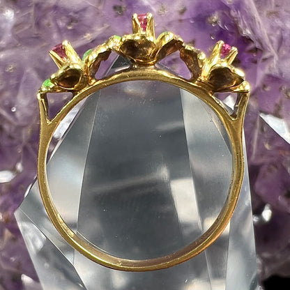 A gold ladies' ring in the motif of three flowers set with round ruby centers and green enameled petals.