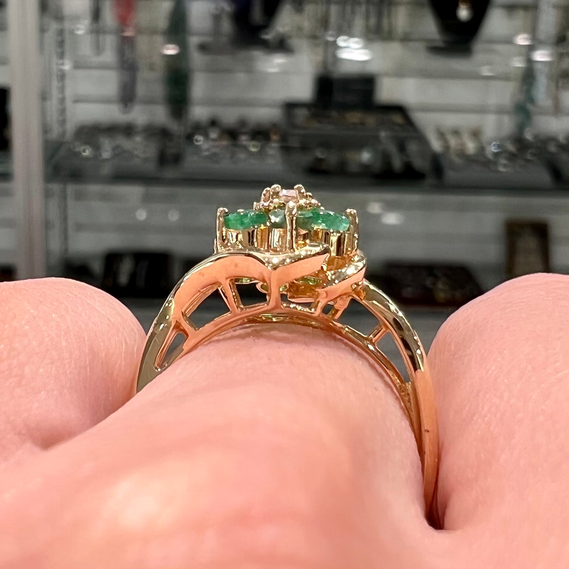 A yellow gold ring set with round cut emerald and diamonds that form the shape of two flowers.