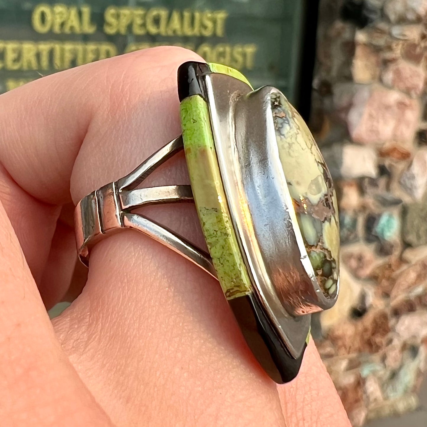 A shield shaped silver ring bezel set with a green gaspeite stone with stone inlaid edges, handmade by artist Benny Armijo.