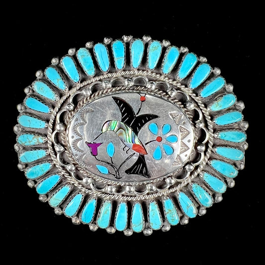 A unisex sterling silver belt buckle featuring the motif of a stone inlaid hummingbird set with petit point turquoise accents, handmade by Navajo artist, Leo G. Harvey.