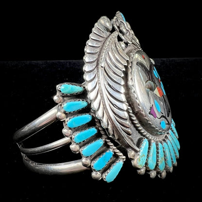 A sterling silver cuff bracelet featuring the motif of a stone inlaid hummingbird with petit point turquoise accents, handmade by Navajo artist Leo G. Harvey.