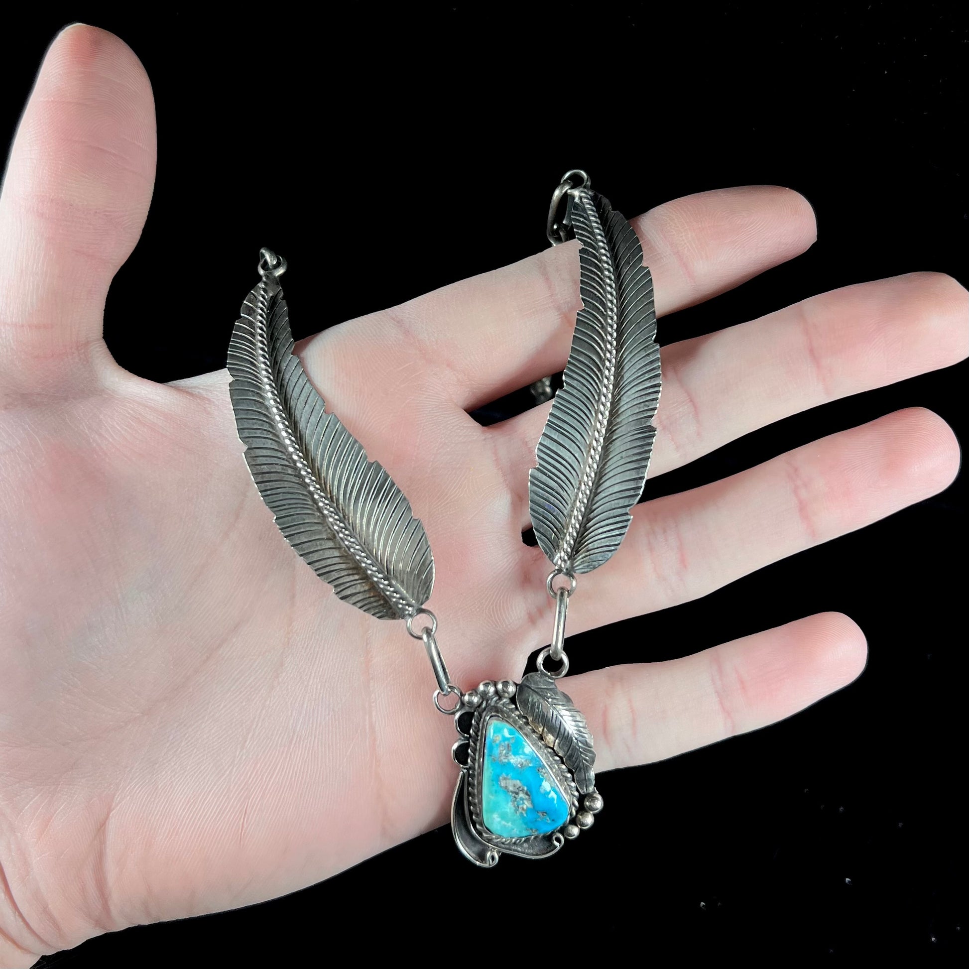 A sterling silver feather motif necklace set with a Sleeping Beauty turquoise stone, handmade by Navajo artist, Jameson Lee.