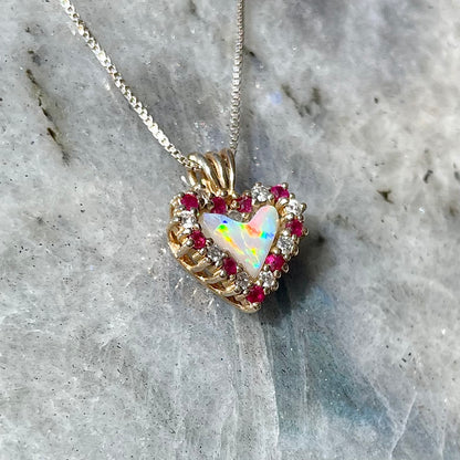 A yellow gold pendant set with a heart cut white opal in a halo of alternating round rubies and diamonds.