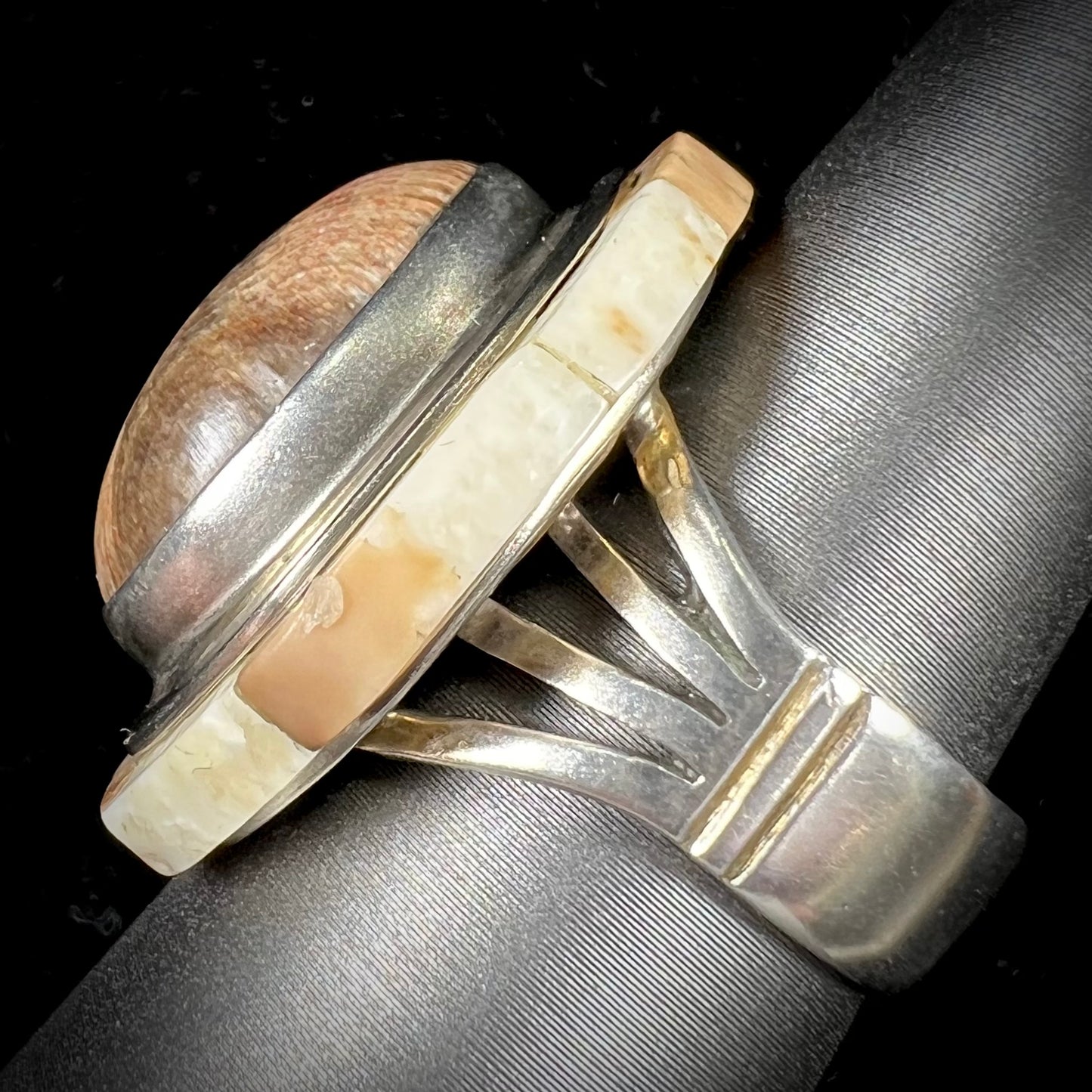 A silver ring handmade from a bezel set petrified wood stone, surrounded by quartz, carnelian, and bone inlay.