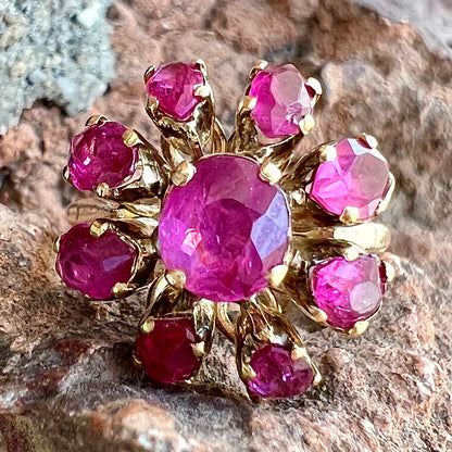 A yellow gold pink Burma ruby cluster ring with a faceted oval center stone surrounded by marquise cut stones.