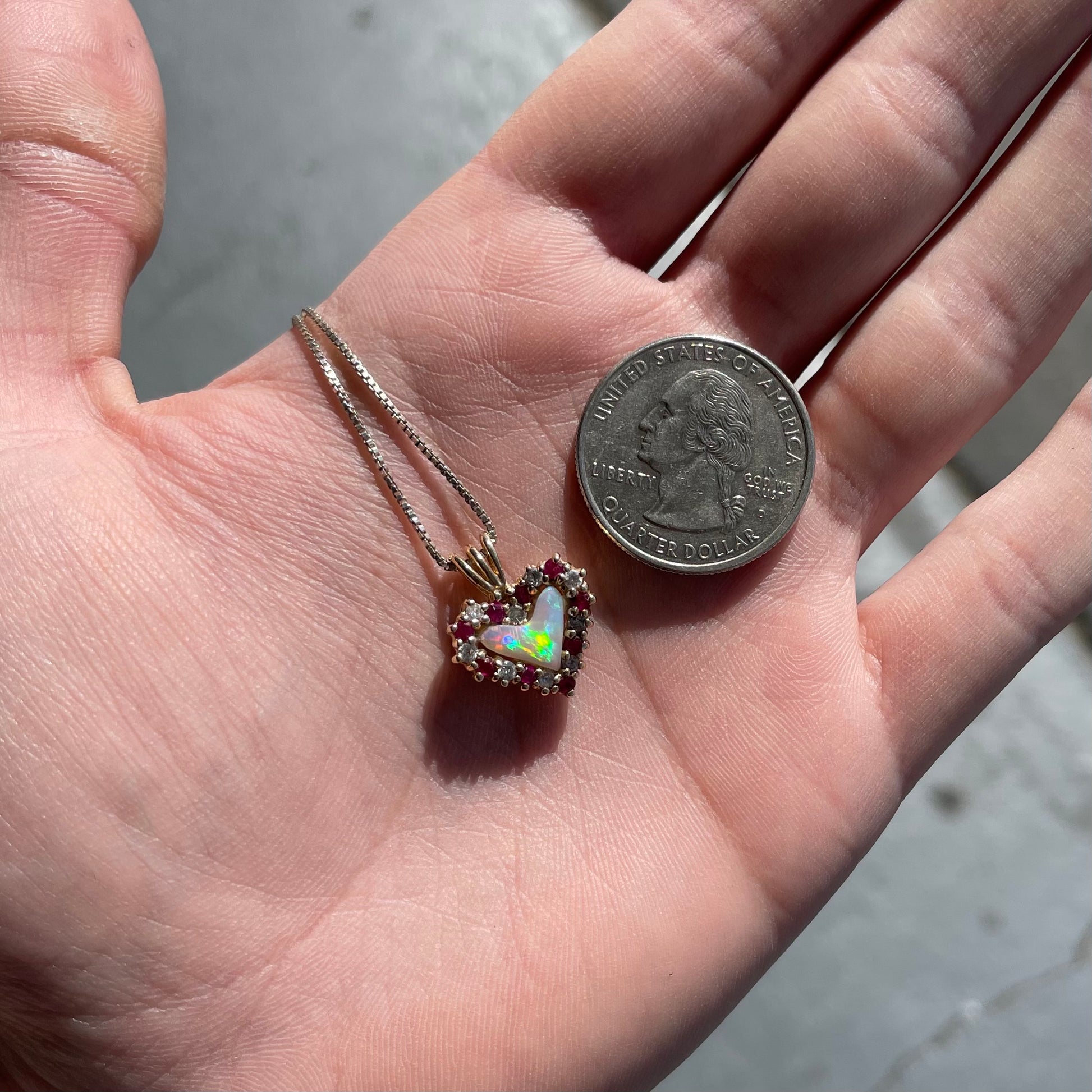 A yellow gold pendant set with a heart cut white opal in a halo of alternating round rubies and diamonds.
