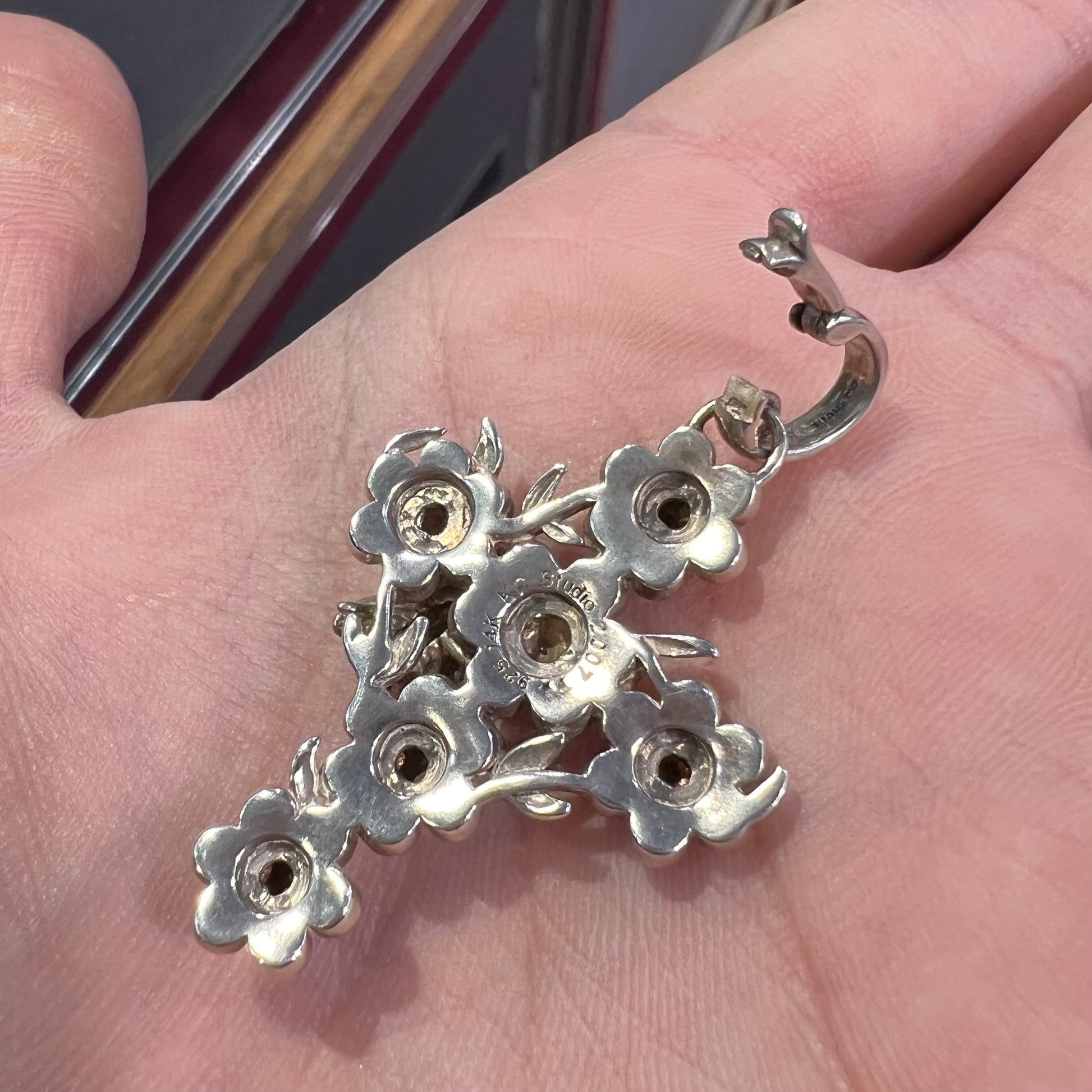 A cross pendant with floral decoration.  The cross is made of six  flowers with sterling silver petals and yellow gold nectar.  A silver bee is on one of the pendants.  The bail opens and closes.