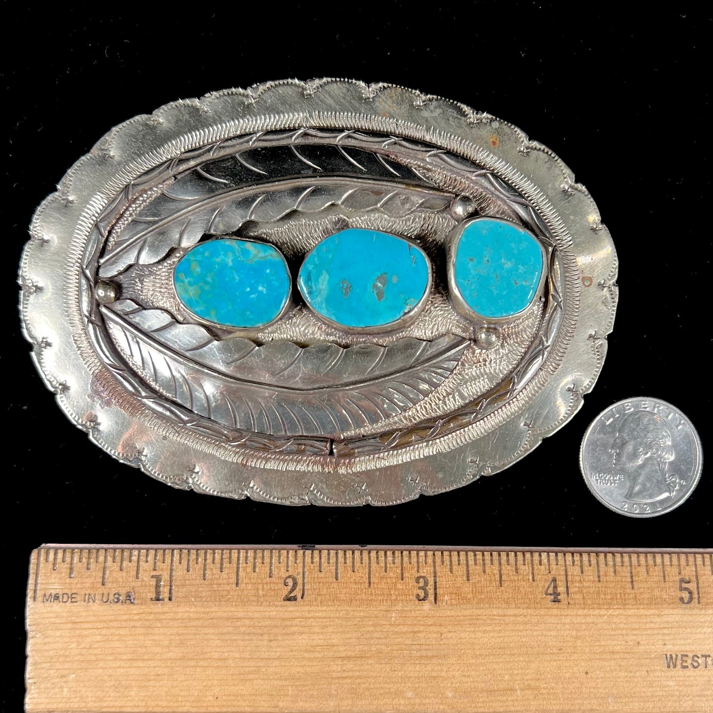 A vintage men's Navajo-made three stone turquoise belt buckle.  The belt buckle is base metal and has a feather design.